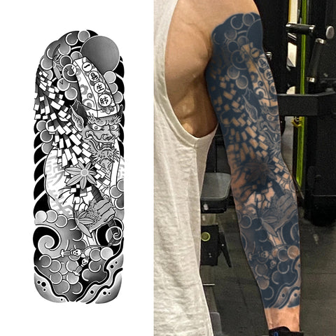Black and white tattoo design on a skateboard deck, with a person wearing a sleeve tattoo in the background.