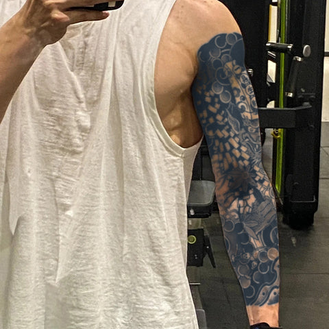 Person taking a selfie with a tattooed arm in a gym setting